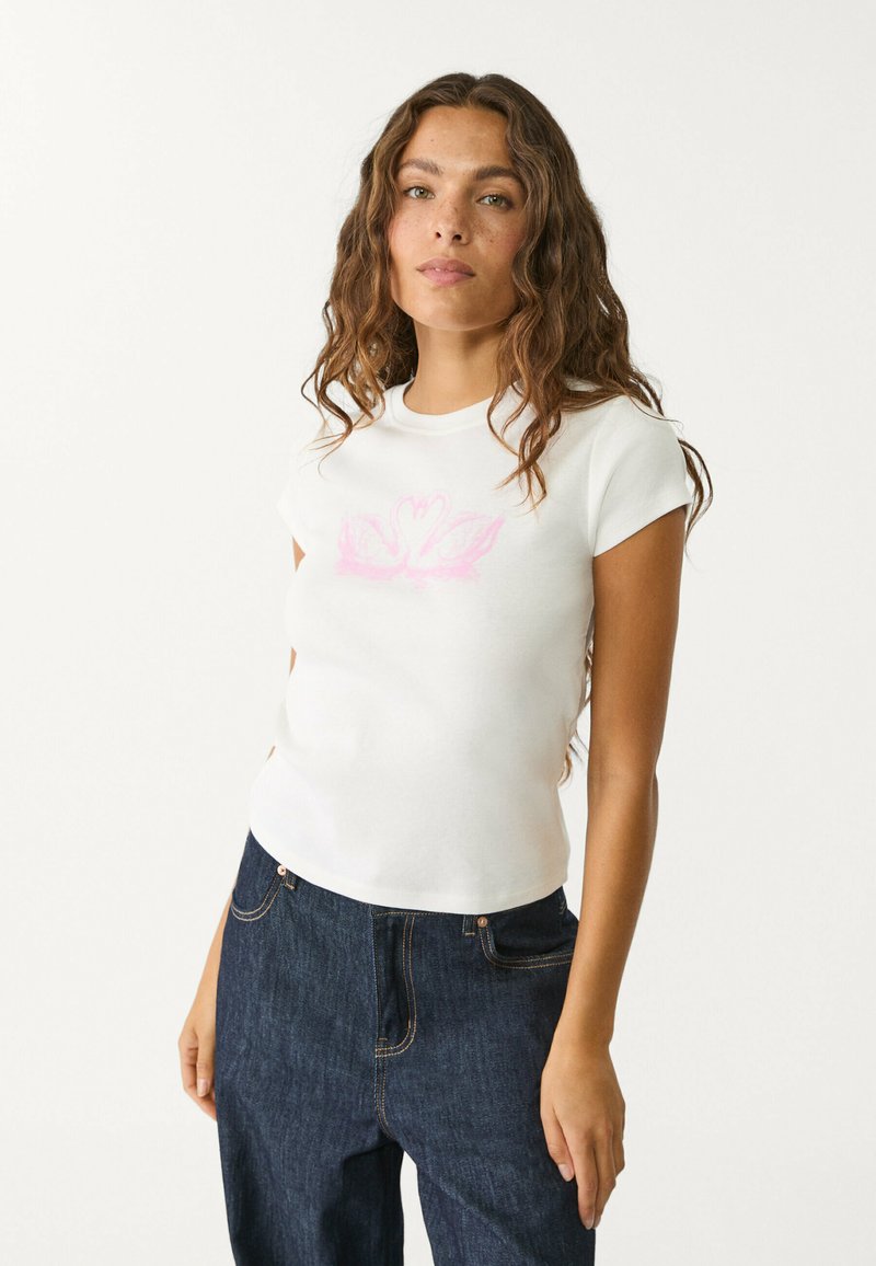 Biała bawełniana koszulka z krótkim rękawem, ozdobiona różową grafiką łabędzia, dopasowana, w połączeniu z ciemnoniebieskimi dżinsami.