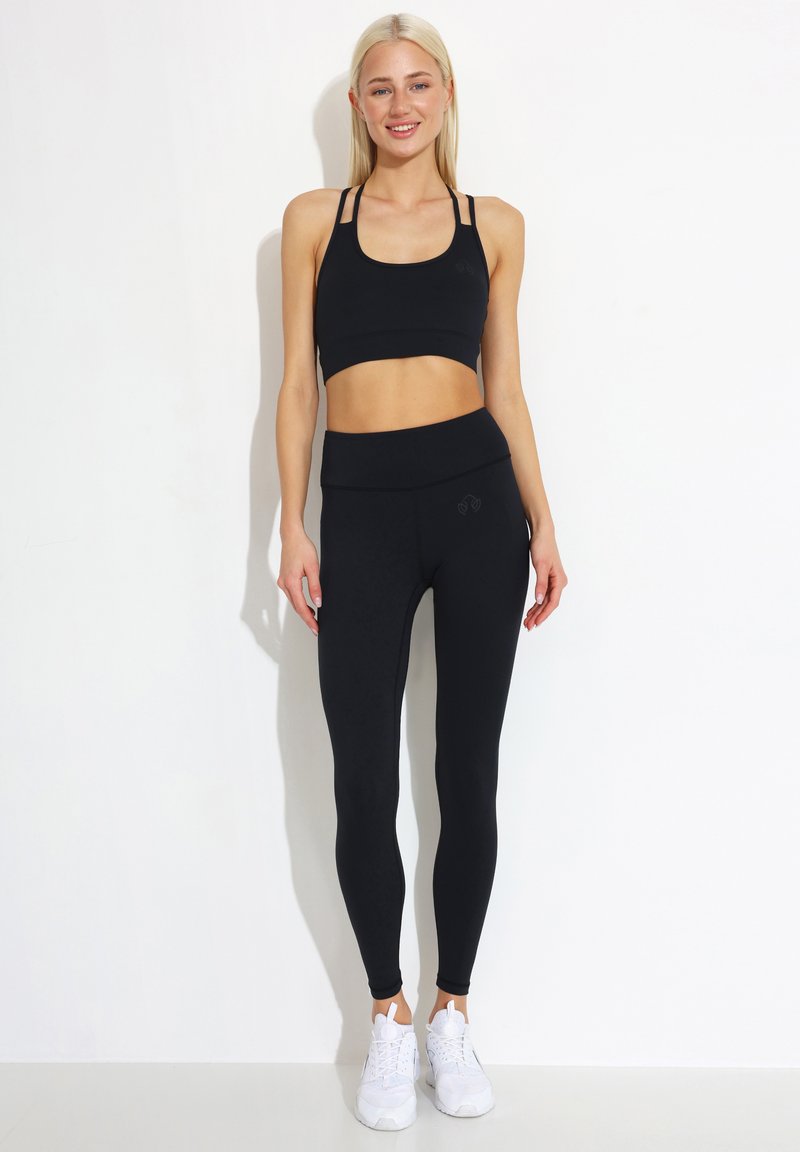 Sutien sport negru cu bretele ajustabile și colanți negri cu talie înaltă. Ținuta este confectionată dintr-un material elastic, asortată cu încălțăminte sport albă.