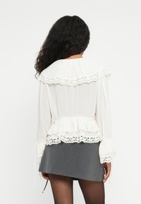 Witte blouse met gerimpelde kanten kraag en manchet, met eenGathered taille en doorschijnende stof. gedragen met een grijze rok.
