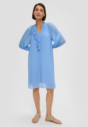 Robes plissées bleu clair avec de longues manches ballon et des détails de col en volants. Portée avec des sandales plates à lanières sur un fond neutre.