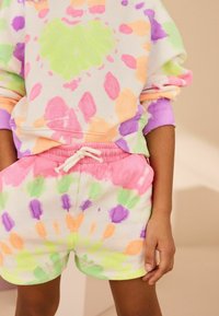 Ensemble de sweatshirt et short tie-dye coloré. Présente des motifs vibrants en rose, vert, orange et violet sur un tissu blanc avec des poignets côtelés.