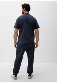 Navy Baumwoll-T-Shirt mit kurzen Ärmeln, kombiniert mit passenden Hosen mit elastischen Bündchen und seitlichen Taschen, getragen mit leichten Schuhen.
