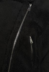 Black fleece jacket featuring a textured surface, two zippers, one vertical and one horizontal, with silver hardware accents.