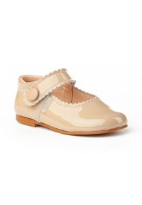 Zapato Mary Jane de charol beige con borde festoneado, correa ajustable, acento de botón circular y suela plana marrón.