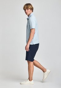 Camisa polo azul claro con mangas cortas, combinada con pantalones cortos azul marino. Zapatillas blancas. Textura suave y corte clásico. Diseño sencillo.