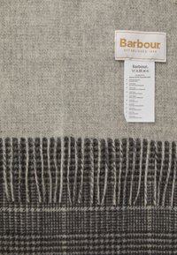Écharpe en laine beige et gris foncé avec un bord frangé et une étiquette Barbour blanche indiquant les instructions d'entretien et les détails du tissu.
