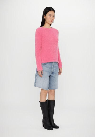 Suéter de punto rosa suave, pantalones cortos de mezclilla y botas negras de tacón alto hasta la rodilla, con un ajuste relajado y dobladillos cortos deshilachados.