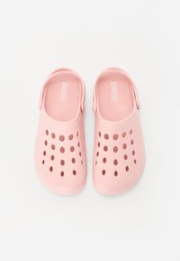 Pink plastic clogs with perforated uppers, molded footbeds, and adjustable heel straps, featuring a smooth texture and lightweight design.
