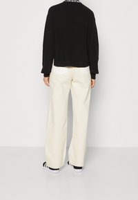 Czarny dziany sweter o prążkowanej fakturze. Połączony z kremowymi spodniami o szerokich nogawkach z białymi naszywanymi kieszeniami oraz butami w czarno-białe paski.