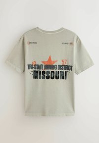 Hellgraues T-Shirt mit schwarzem und orangem Text, der "Tri-State Mining District Missouri" sowie die Zahlen "18" und "57" mit einem orangenen Stern zeigt.