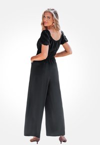 Černý overal s krátkými nabíranými rukávy, tvarovaným pasem a širokými nohavicemi. Hladká textura, jednobarevný a jednoduchý, elegantní silueta.