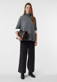 Grauer Rollkragenpullover mit lockerer Passform und geripptem Saum, kombiniert mit weit geschnittenen schwarzen Hosen und einer dunkelbraunen Clutch. Schwarze Stiefel mit Absatz.