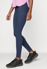 Κολάν σε ναυτικό μπλε με λεία υφή, διακοσμημένο με οριζόντιες ραβδώσεις στα πλάγια, συνδυασμένο με μαύρα αθλητικά παπούτσια από δίχτυ.