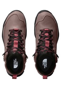 Botas de senderismo marrones con suelas negras, con detalles en rosa y cordones negros. El interior muestra un logotipo en una plantilla negra.