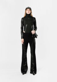 Body negro de manga larga y cuello alto, con detalles de cuero brillante, combinado con pantalones negros acampanados y tacones de punta.