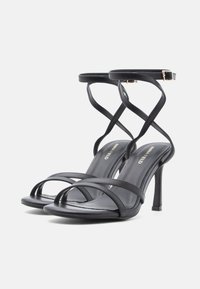 Mustad kõrge kontsaga sandaalid mitme õhukese rihmaga, siidise tekstuuriga ja terava otsaga. Varustatud reguleeritava pahkluurihmaga ja stiletto kontsaga.