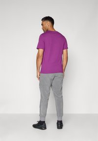 Moška vijolična bombažna majica s kratkimi rokavi, v kombinaciji s sivo športnimi hlačami z stranskimi žepi. Črni superge z zelenimi akcenti.