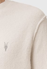 Hellbeige gestrickter Pullover mit geripptem Muster, auf der linken Brust mit einem dezenten gestickten Ziegenschädel versehen. Klassisches Rundhals-Design.