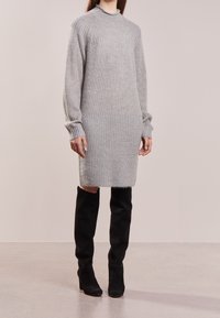 Robe tricotée grise avec texture côtelée, manches longues et col montant, associée à des bottes en daim noir montant jusqu'aux genoux.