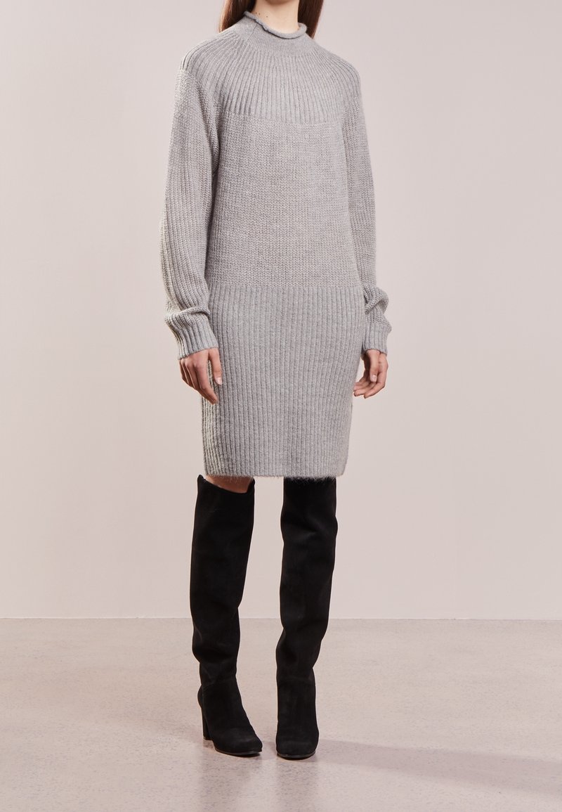 Robe tricotée grise avec texture côtelée, manches longues et col montant, associée à des bottes en daim noir montant jusqu'aux genoux.