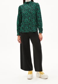 Groene en zwarte geblokte blouse met lange mouwen, gecombineerd met wijde zwarte broeken en witte sneakers met gele veters.
