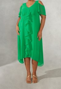 Grön chiffongklänning med V-ringning, volangdetalj fram, korta axelbandsärmar och en hög-låg fåll. Guldiga sandaler fulländar looken.
