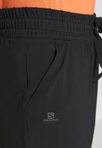 Svarta atletiska shorts tillverkade av lättviktsmaterial med elastisk midja och snörning, med en sidoficka och en logopåskrift.