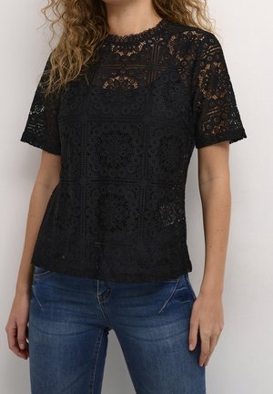 Zwarte kant top met korte mouwen, een geschulpte halslijn en complexe florale patronen. Gecombineerd met blauwe spijkerbroeken voor contrast.