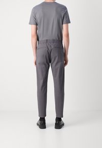 Grå bomullst-shirt och kolgrå byxor med elastisk midjeband, bakfickor. Svarta skor med röda detaljer vid hälen.