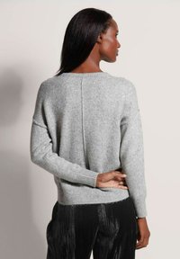 Helles graues Sweatshirt aus weichem Material mit rundem Halsausschnitt, gerippten Ärmelbündchen und einer Rückennaht, kombiniert mit schwarzen, strukturierten Hosen.