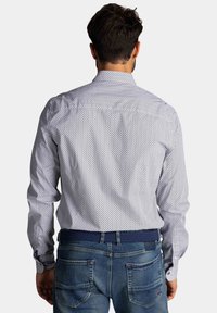 Witte shirt met kleine blauwe geometrische patronen, met knoopsluiting en lange mouwen, gecombineerd met een blauwe spijkerbroek en een blauwe geweven riem.