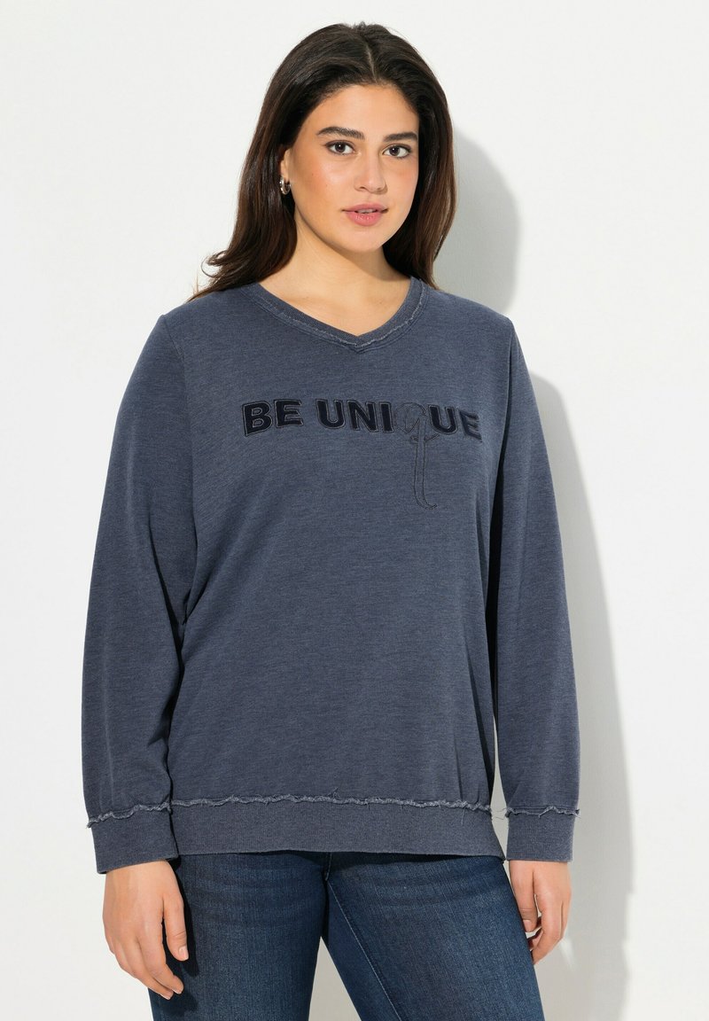 Navyblauer Pullover mit V-Ausschnitt, versehen mit der schwarzen Stickerei "BE UNIQUE". Weicher Stoff, lockere Passform und fransige Saumdetails.