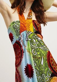 Robe dos nu colorée présentant un mélange de motifs paisley et abstraits dans des tissus verts, rouges, orange et bleus avec une texture fluide.