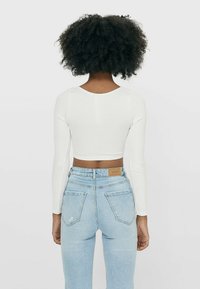 Weißes geripptes Langarm-Crop-Top kombiniert mit hellblauen hoch taillierten Jeans, die ein körperbetontes Design und eine mittlere Taille zeigen.