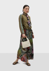 Olive green button-up shirt with striped sleeves, patterned maxi skirt in vibrant colors, white handbag with a cork handle, and strappy sandals.