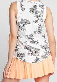 Haut blanc sans manches avec des scènes détaillées de nature et d'animaux en noir, associé à une mini-jupe plissée pêche sur une personne debout.