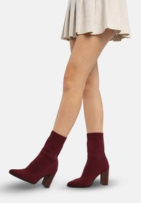 Botines burdeos hechos de material de punto elástico, con puño acanalado, punta puntiaguda y tacón grueso y resistente.