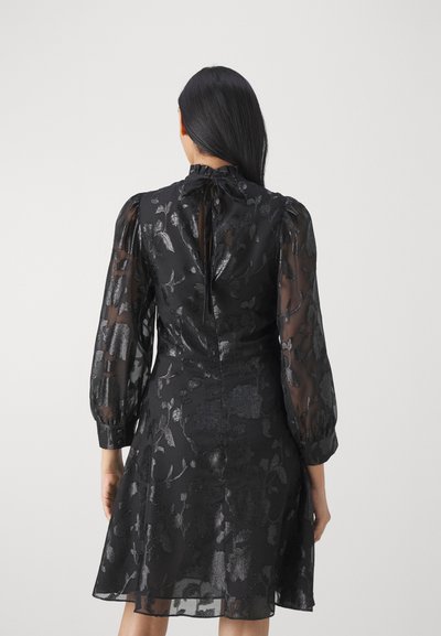 Robe noire à motif floral dotée de manches bouffantes transparentes avec un col volanté, d'un tissu texturé et d'un ourlet évasé. Fermeture à l'arrière avec des boutons.