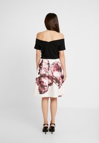 Svart off-shoulder topp kombinerad med en knälång vit kjol med ett rosa blommönster. Svarta högklackade sandaler kompletterar looken.