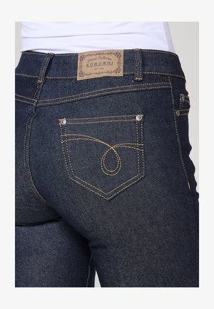Dunkelblaue Denim-Jeans verfügen über einen klassischen Schnitt mit einer hohen Taille, kontrastierenden gelben Nähten und einem auffälligen Design der Gesäßtasche.