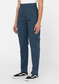 Blå byxor med hög midja och rak passform, utrustade med sidofickor och synliga söm detaljer, kombinerade med svartvita sneakers.