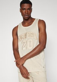 Maillot de basketball en mesh beige avec "NEW ERA" et "20" imprimés en beige. Doté d'un col rond et d'un design sans manches, texturé pour la respirabilité.