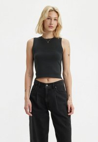 Svart ärmlös kort topp med ribbad textur. Kombinerad med högmidjade svarta denimjeans. Enkelt design utan synliga mönster eller accenter.