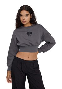 Szary, krótki sweatshirt z długimi rękawami, z czarnym nadrukiem w kształcie ust i napisem "Więcej miłości, proszę", w połączeniu z czarnymi spodniami typu cargo.