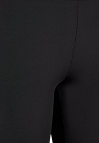 Juodos leggingai, pagaminti iš tamprios medžiagos, su lygia tekstūra ir prigludusia forma, su matoma siūle palei šoną.