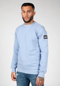 Sudadera azul claro de mezcla de algodón, con cuello redondo, puños acanalados y un parche negro con el logo "WRONG FRIENDS" en la manga.