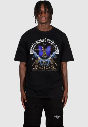 Sort t-shirt med et grafisk design, der viser en blå sommerfugl og skeletter, tekst ovenfor og nedenfor i hvid. Fremstillet af bomuldsmateriale og med korte ærmer.