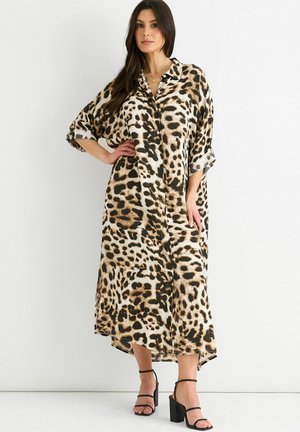 Leopard print maxi dress in lightweight fabric; features button front, oversized fit, and an asymmetrical hem. Black strappy heels complete the look.