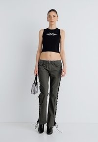 Μαύρο κομμένο τοπ, ελιάς πράσινο παντελόνι με διακοσμητικά δέσιμα στο πλάι, μαύρα μυτερά μποτάκια και μια μικρή ιριδίζουσα τσάντα χειρός.