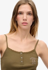 Oliwkowy, prążkowany top bez rękawów z koronkowym obszyciem, z trzema guzikami i białym haftem tekstu "SUPERDRY ATHL 19" na przodzie.